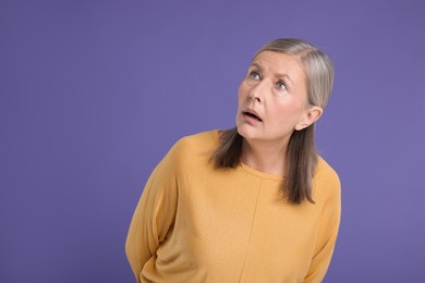 Portrait of surprised senior woman on violet background, space for text