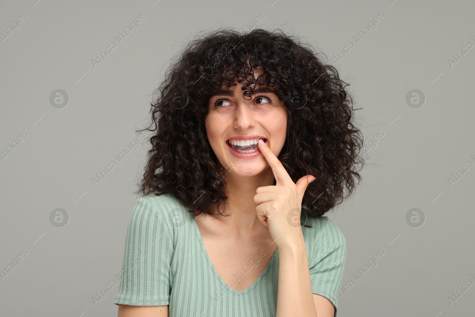 Photo of Young woman applying whitening strip on her teeth against grey background