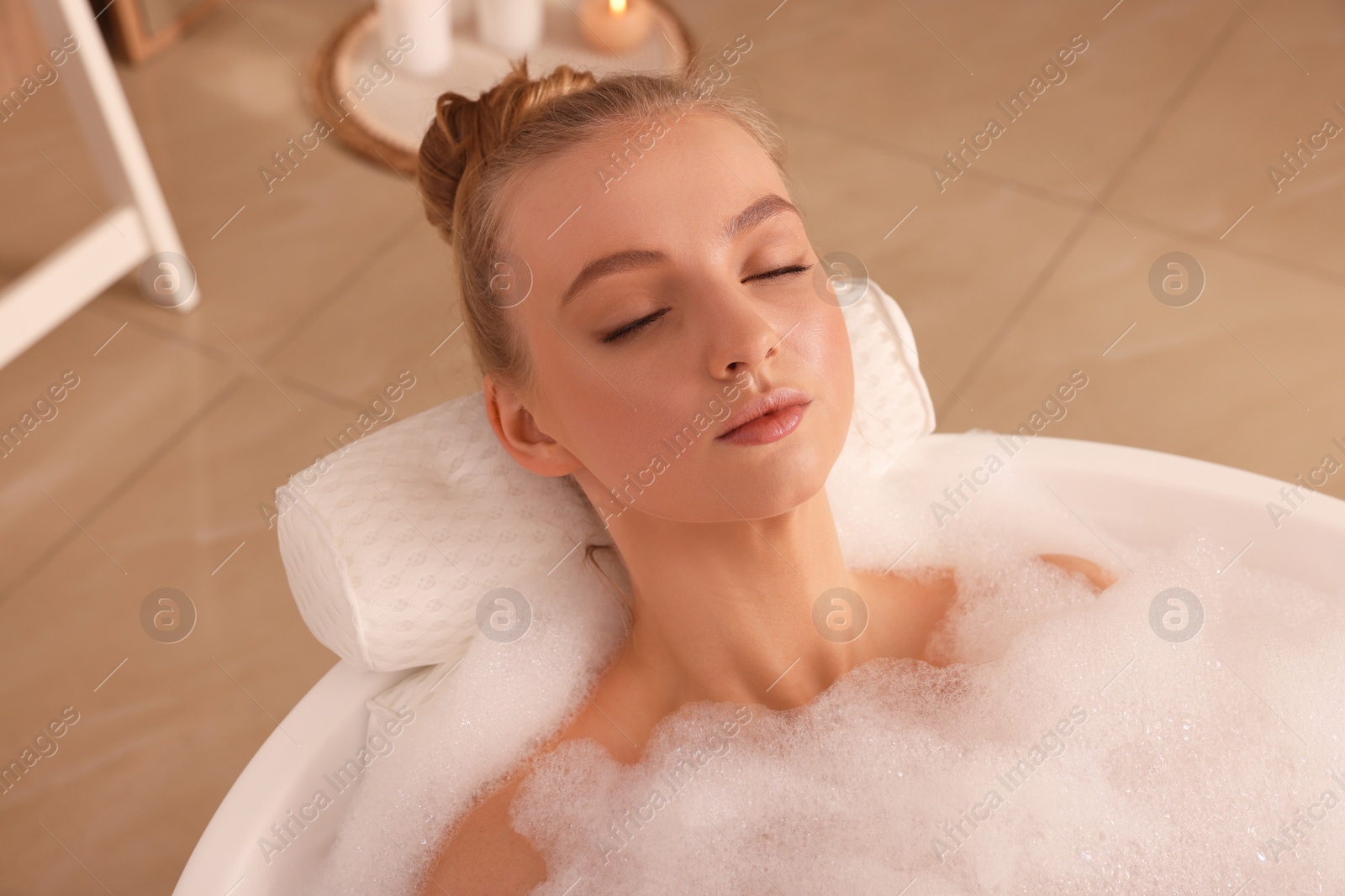 Photo of Young woman using pillow while enjoying bubble bath indoors