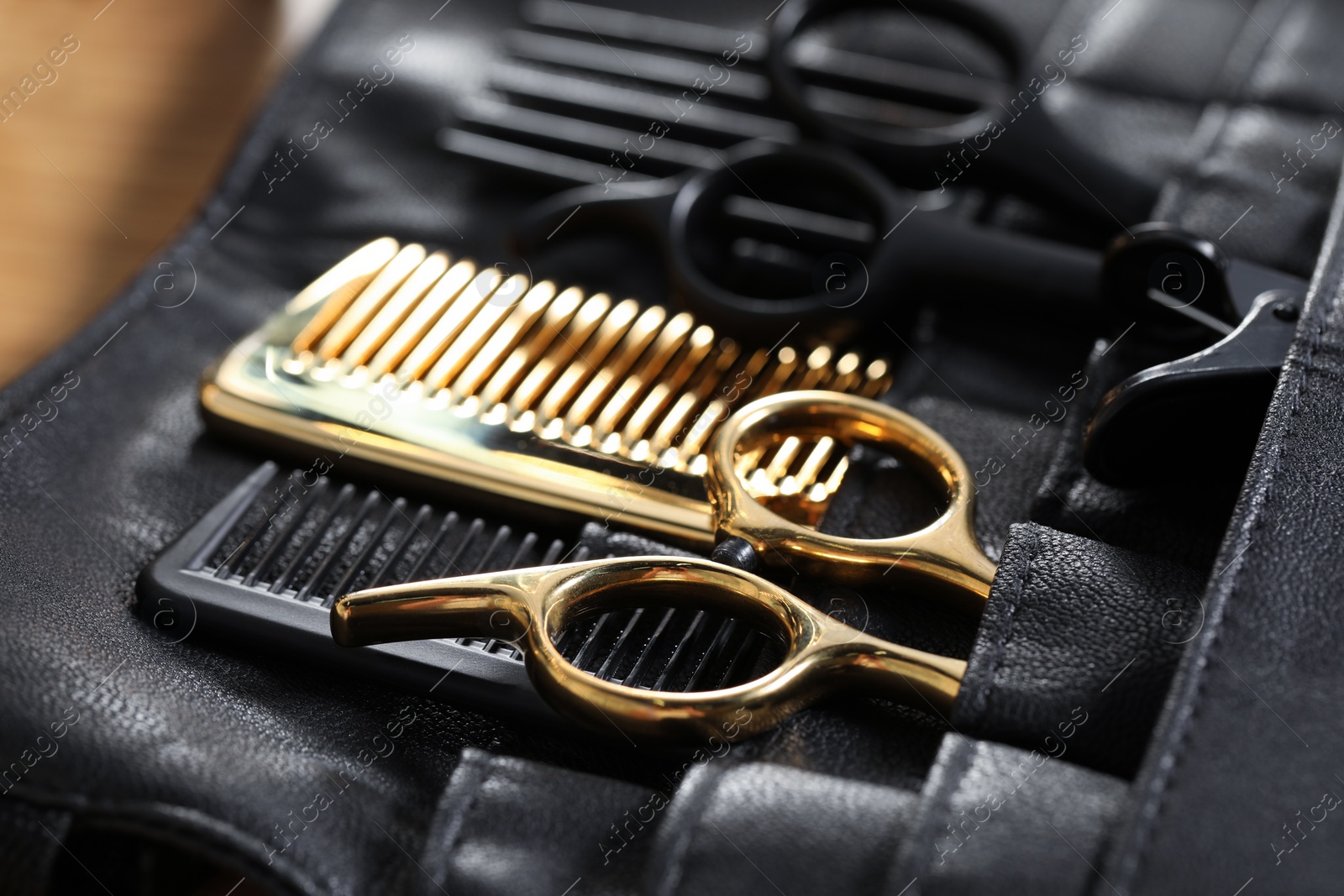 Photo of Hairdresser tools. Professional scissors and combs in leather organizer on wooden table, closeup