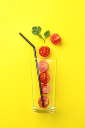 Glass, fresh tomatoes, parsley and straw on yellow background, flat lay