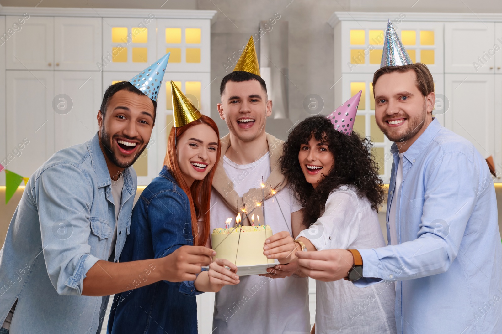 Photo of Happy friends with tasty cake and sparklers celebrating birthday in kitchen