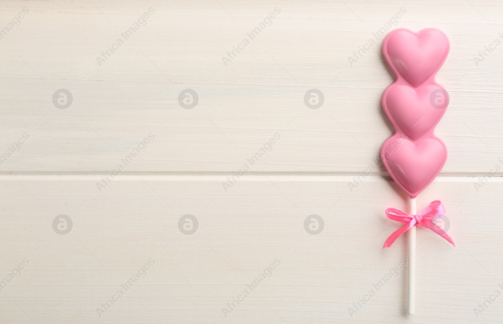 Photo of Chocolate heart shaped lollipop on white wooden table, top view. Space for text