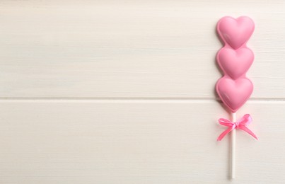 Chocolate heart shaped lollipop on white wooden table, top view. Space for text