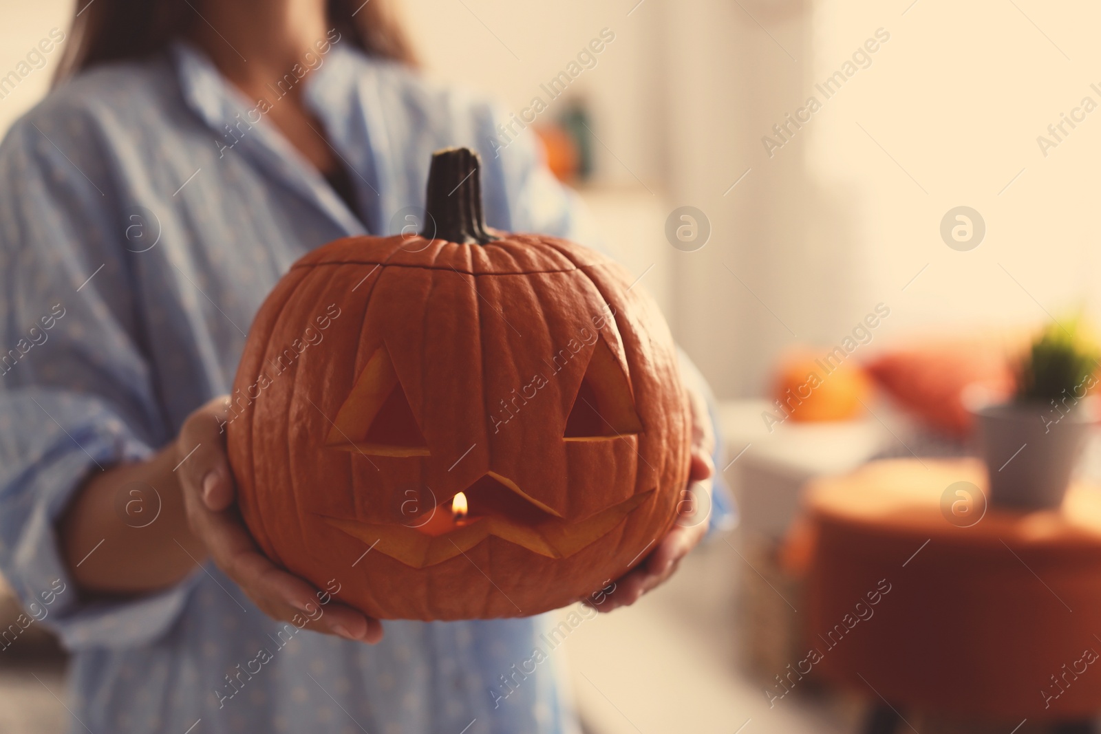 Photo of Woman holding pumpkin jack o'lantern indoors, closeup with space for text. Halloween celebration