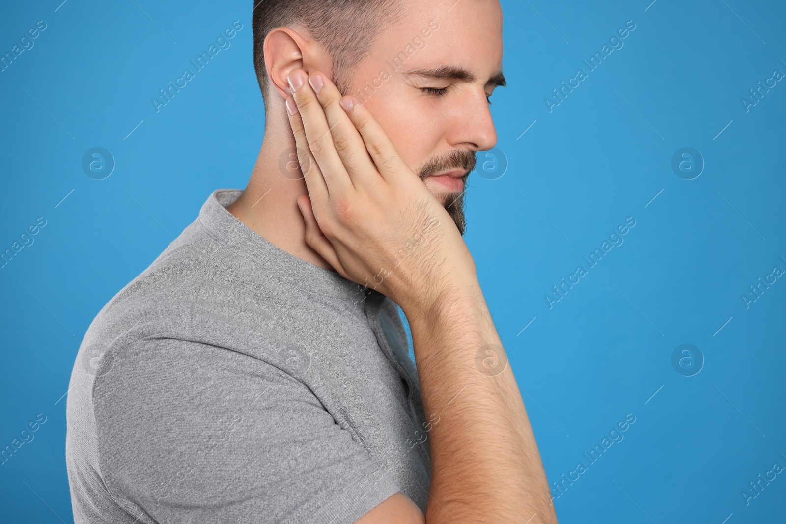 Photo of Young man suffering from ear pain on light blue background