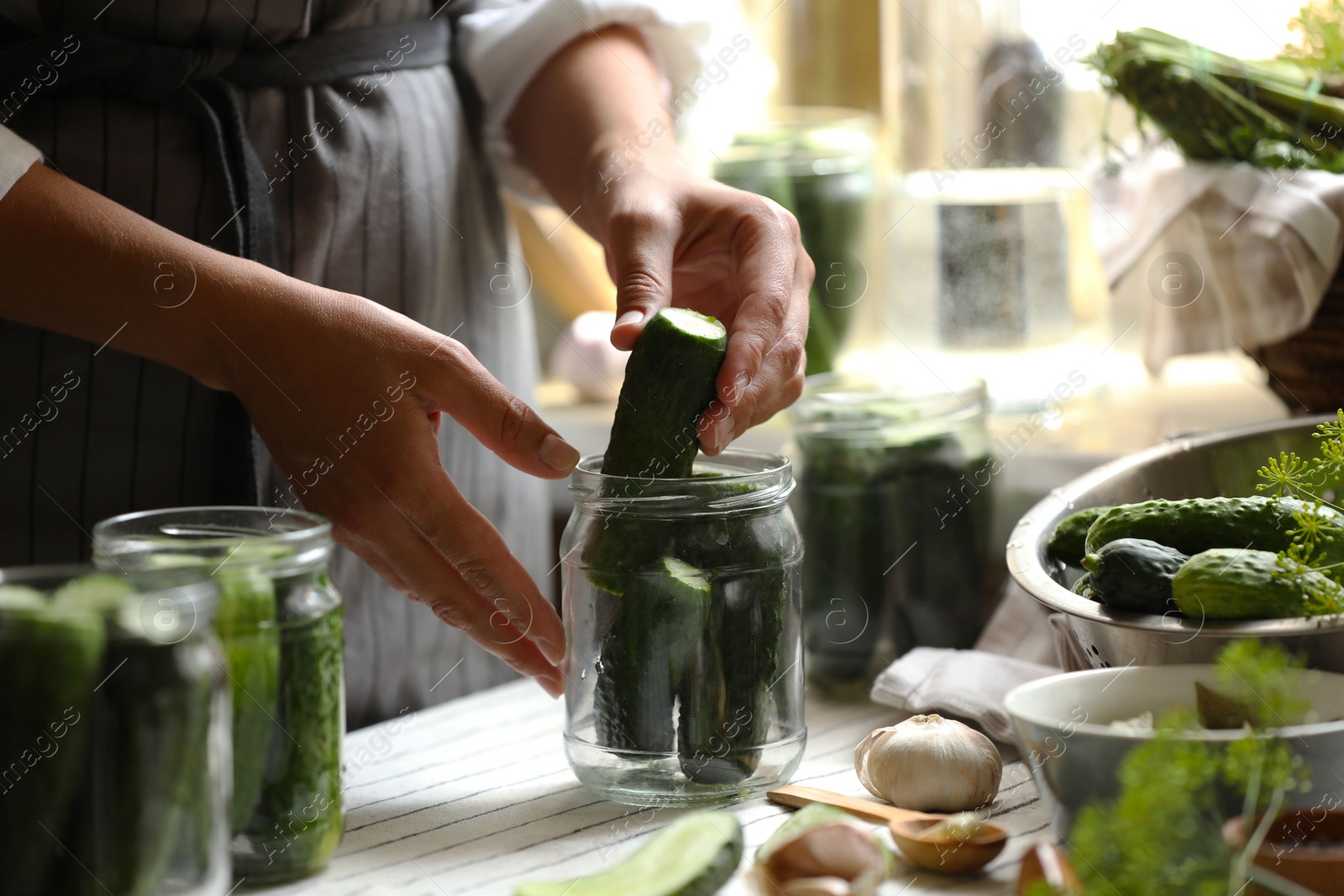 Photo of Woman putting cucumbers into jar in kitchen, closeup. Canning vegetables