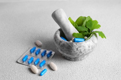 Marble mortar with fresh green herbs and pills on white table, closeup