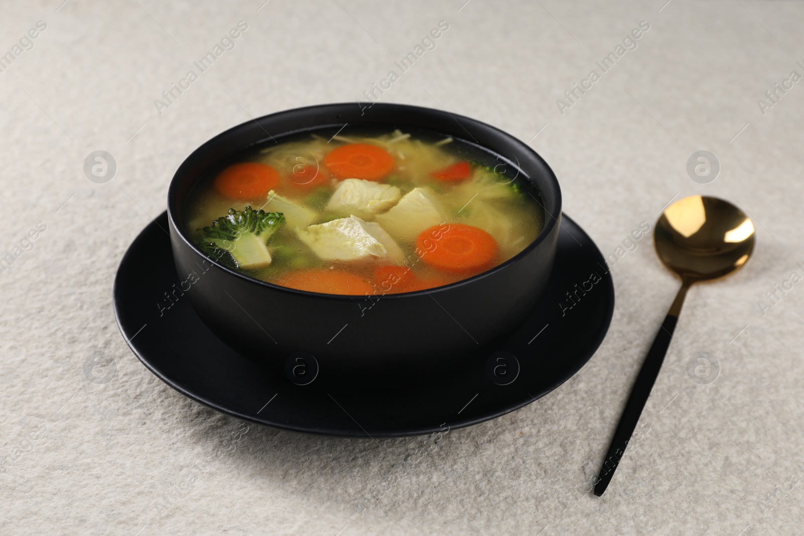 Photo of Tasty chicken soup with noodles and vegetables in bowl served on light textured table