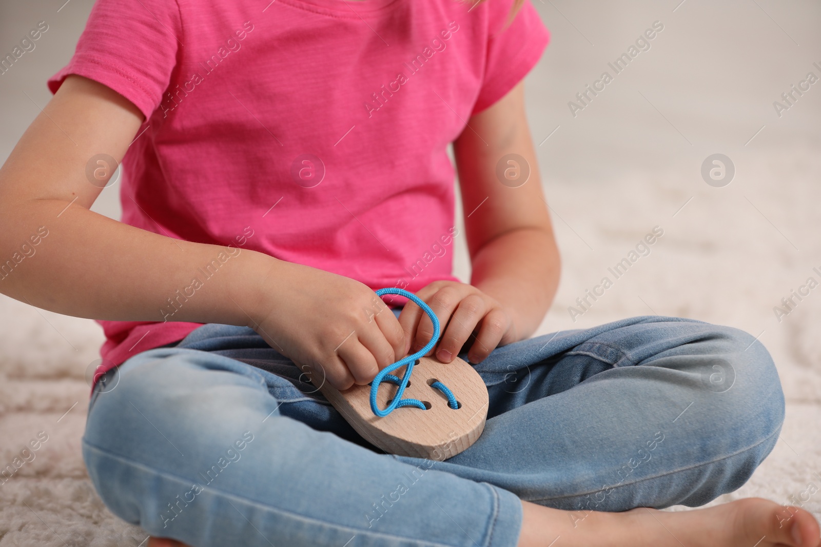 Photo of Little girl playing with wooden lacing toy on carpet indoors, closeup