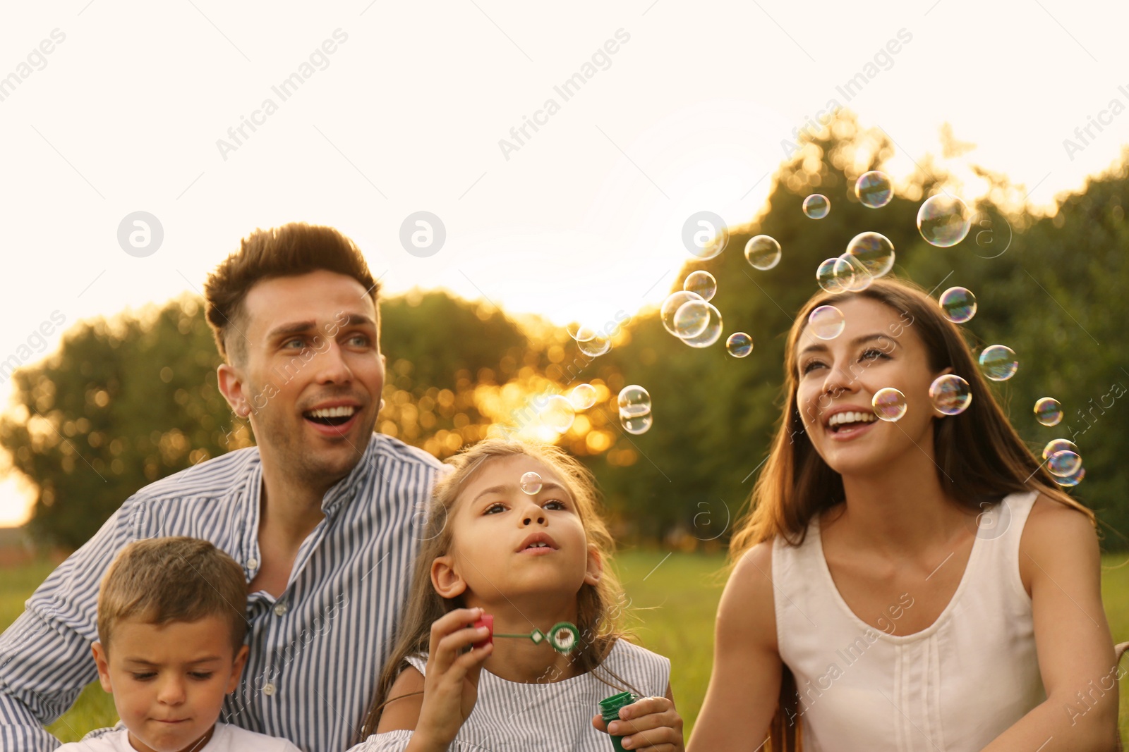 Photo of Happy family blowing soap bubbles in park at sunset. Summer picnic
