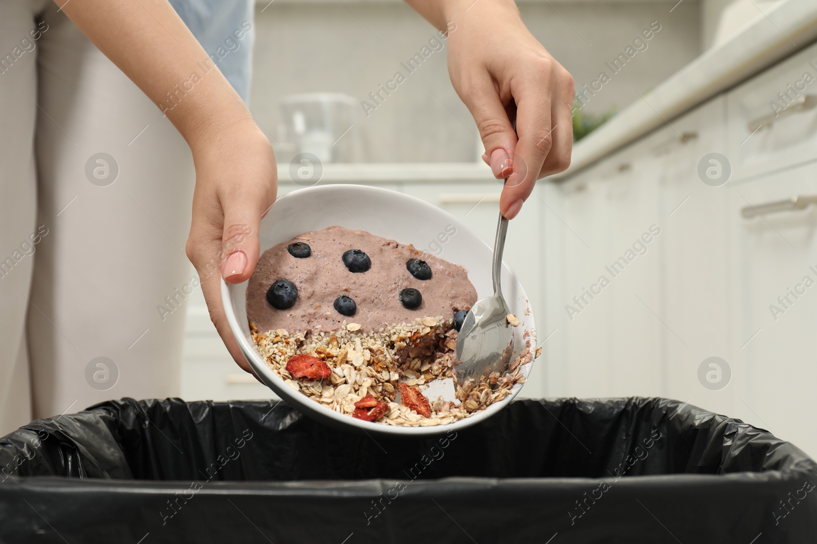 Photo of Woman throwing oatmeal with berries into bin indoors, closeup