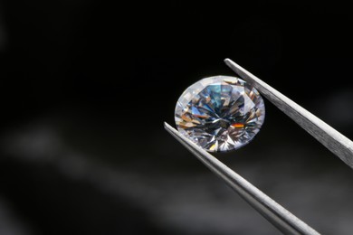 Tweezers with beautiful shiny diamond on dark background, closeup. Space for text