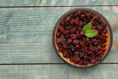 Photo of Tasty dried cranberries and leaves in bowl on blue wooden table, top view. Space for text