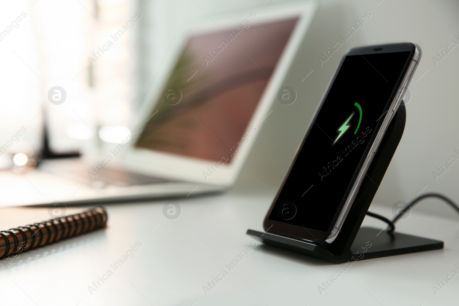 Photo of Mobile phone with wireless charger on white table. Modern workplace accessory