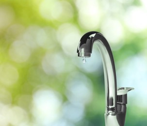 Image of Water drop flowing from tap outdoors on sunny day, bokeh effect
