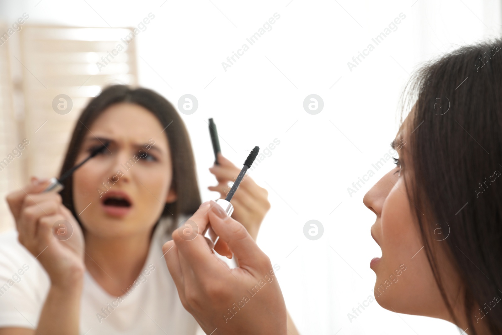 Photo of Beautiful woman holding mascara brush with fallen eyelashes near mirror indoors