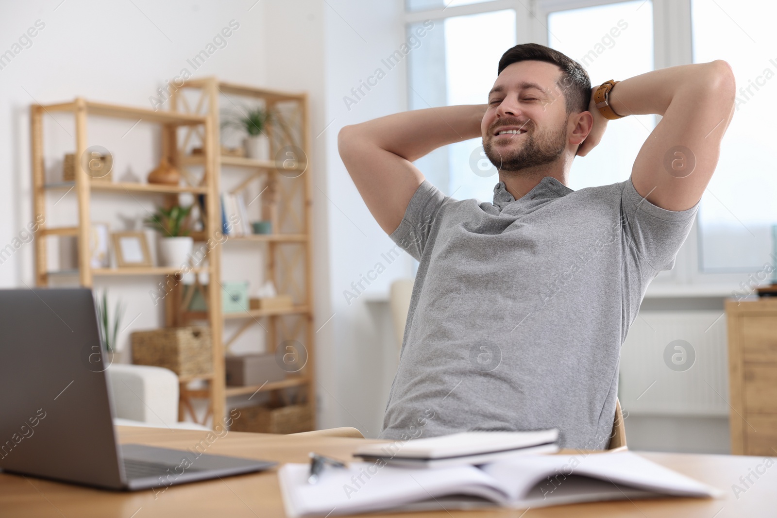 Photo of Happy man having break while working with laptop at wooden desk in room