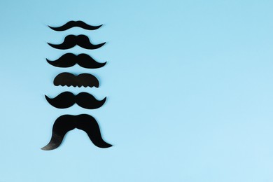 Fake paper mustaches on light blue background, flat lay. Space for text