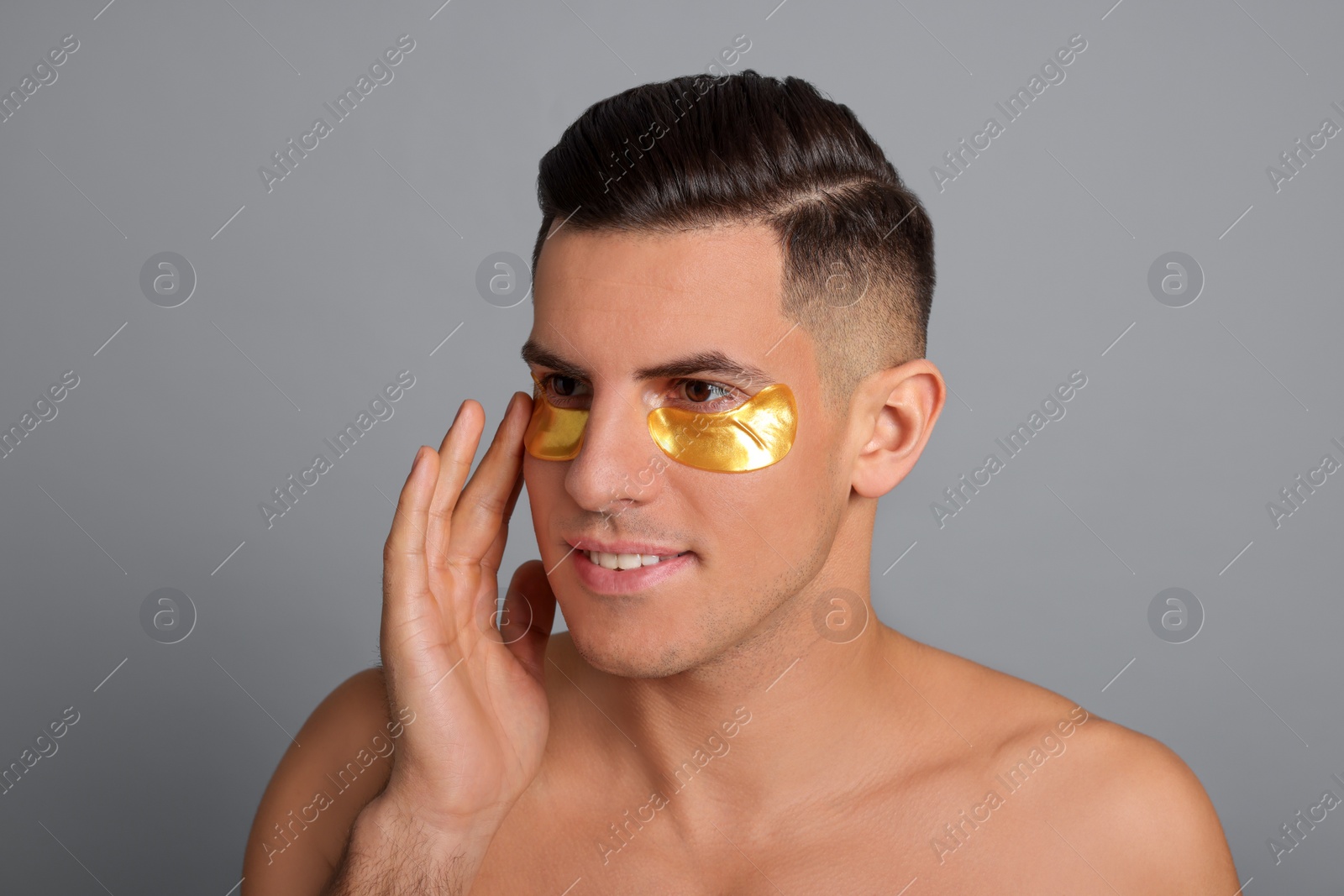 Photo of Man applying golden under eye patch on grey background