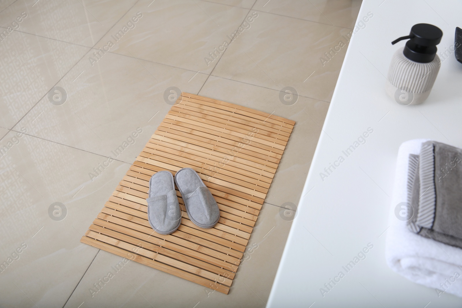 Photo of Wooden mat with slippers on floor in bathroom