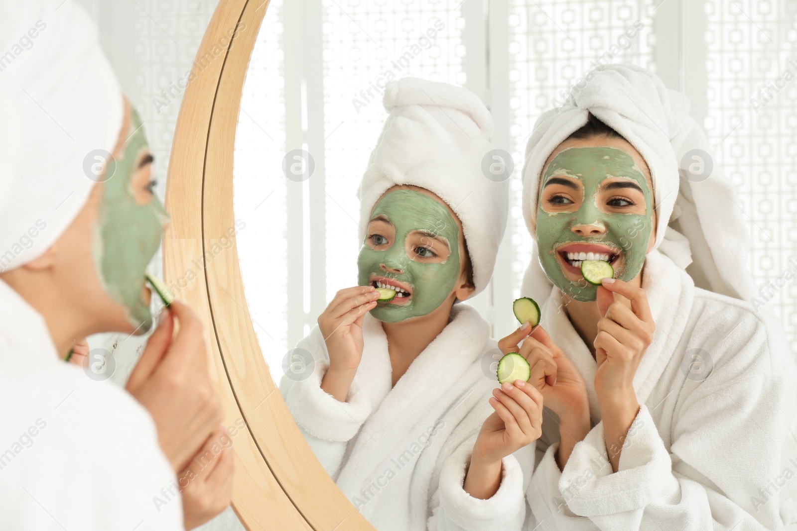 Photo of Young mother and her daughter with facial masks near mirror in bathroom