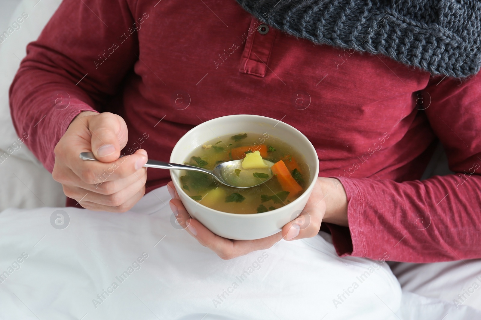 Photo of Sick young man eating broth to cure cold in bed at home