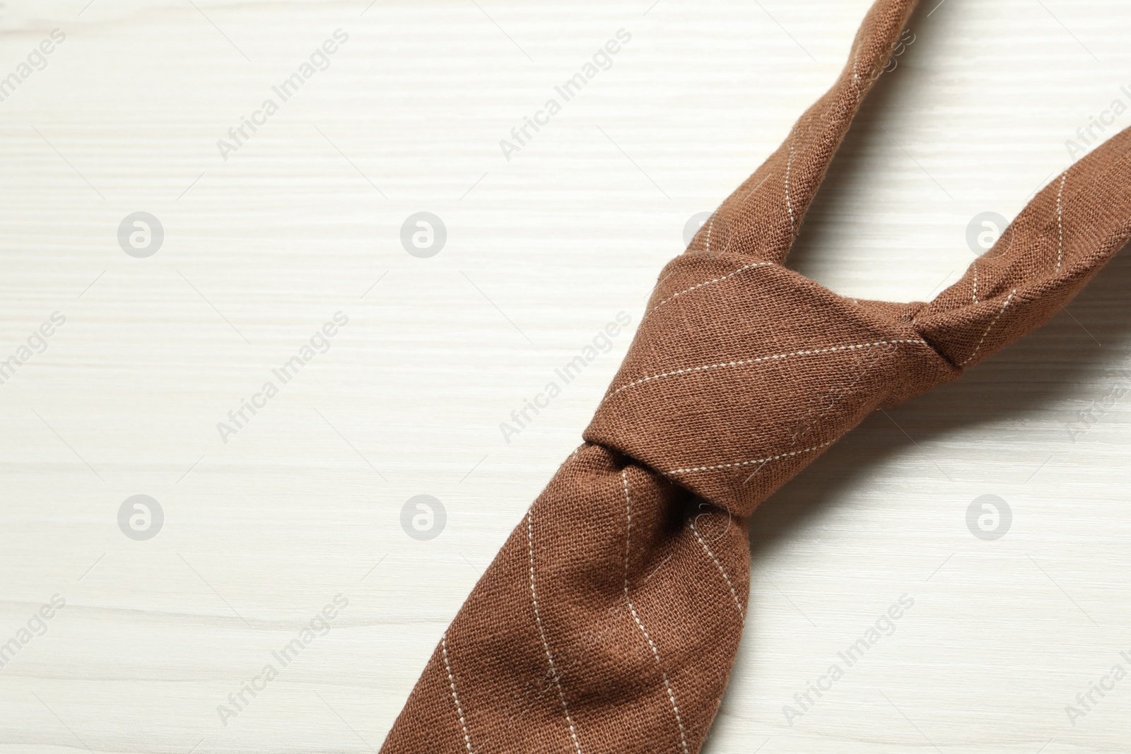 Photo of One striped necktie on white wooden table, top view. Space for text