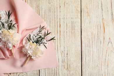 Stylish boutonnieres and pink fabric on light wooden table, top view. Space for text