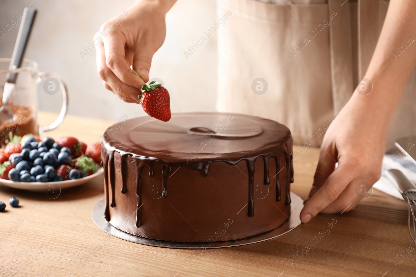 Photo of Baker decorating fresh delicious homemade chocolate cake with berries on table, closeup