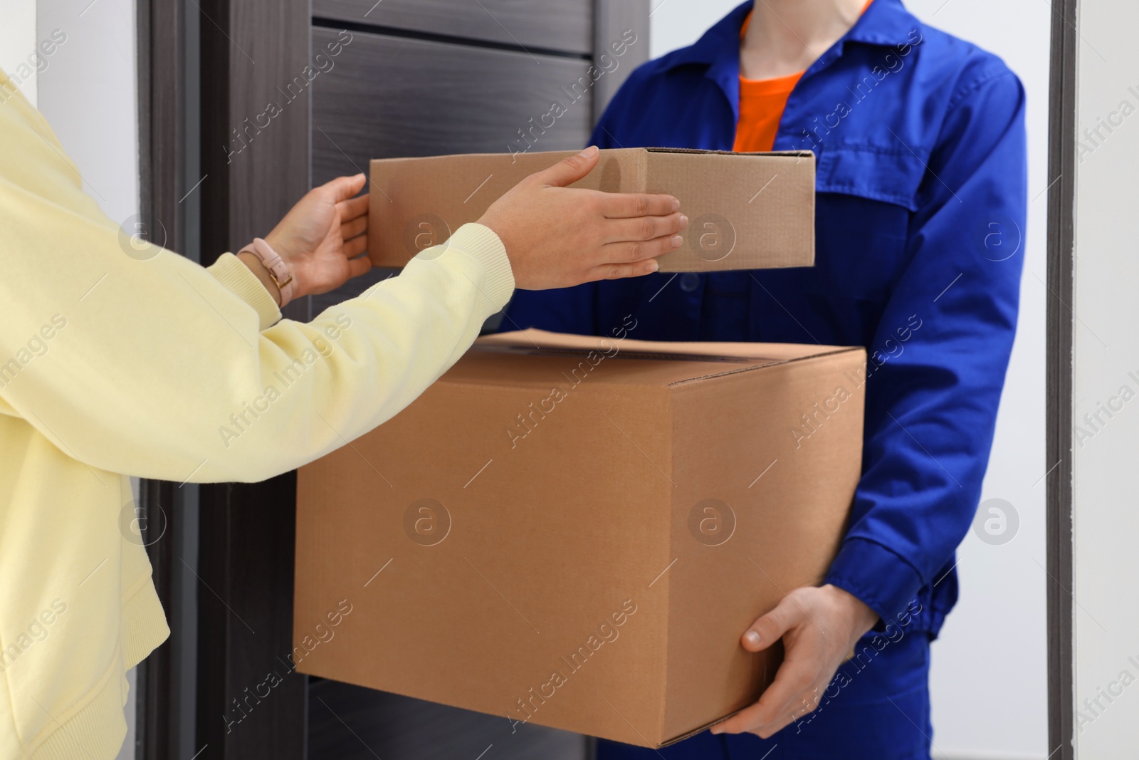 Photo of Courier giving parcels to woman indoors, closeup