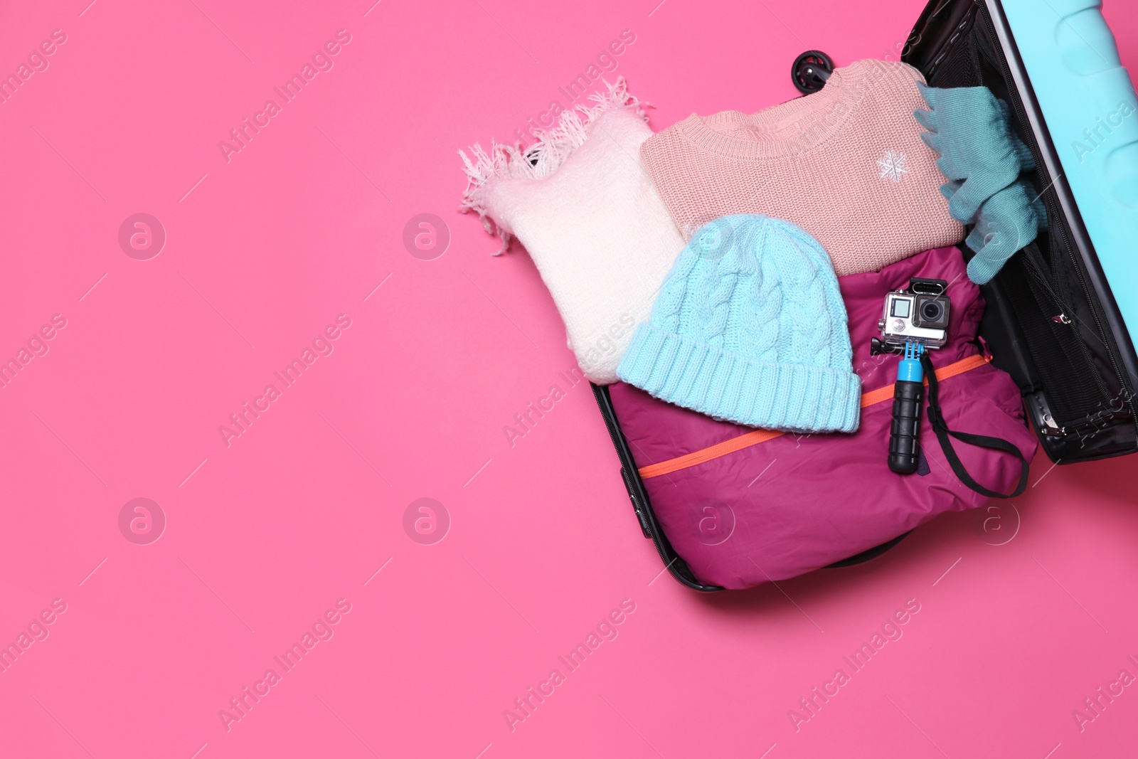 Photo of Warm clothes and action camera in suitcase on color background, top view with space for text. Winter vacation