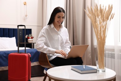 Photo of Beautiful young business woman working with laptop in hotel room