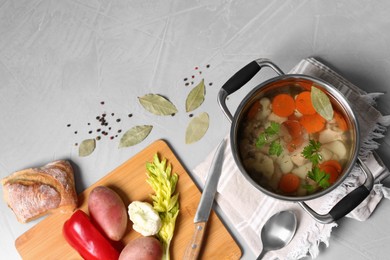 Photo of Pot of delicious vegetable bouillon and ingredients on light grey table, flat lay