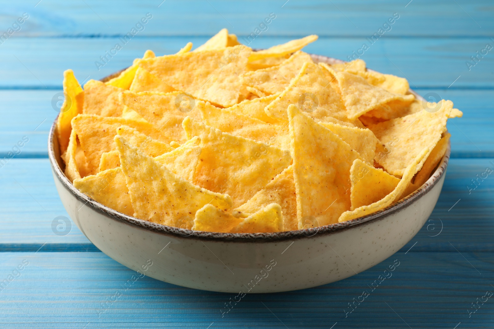 Photo of Tortilla chips (nachos) in bowl on light blue wooden table, closeup