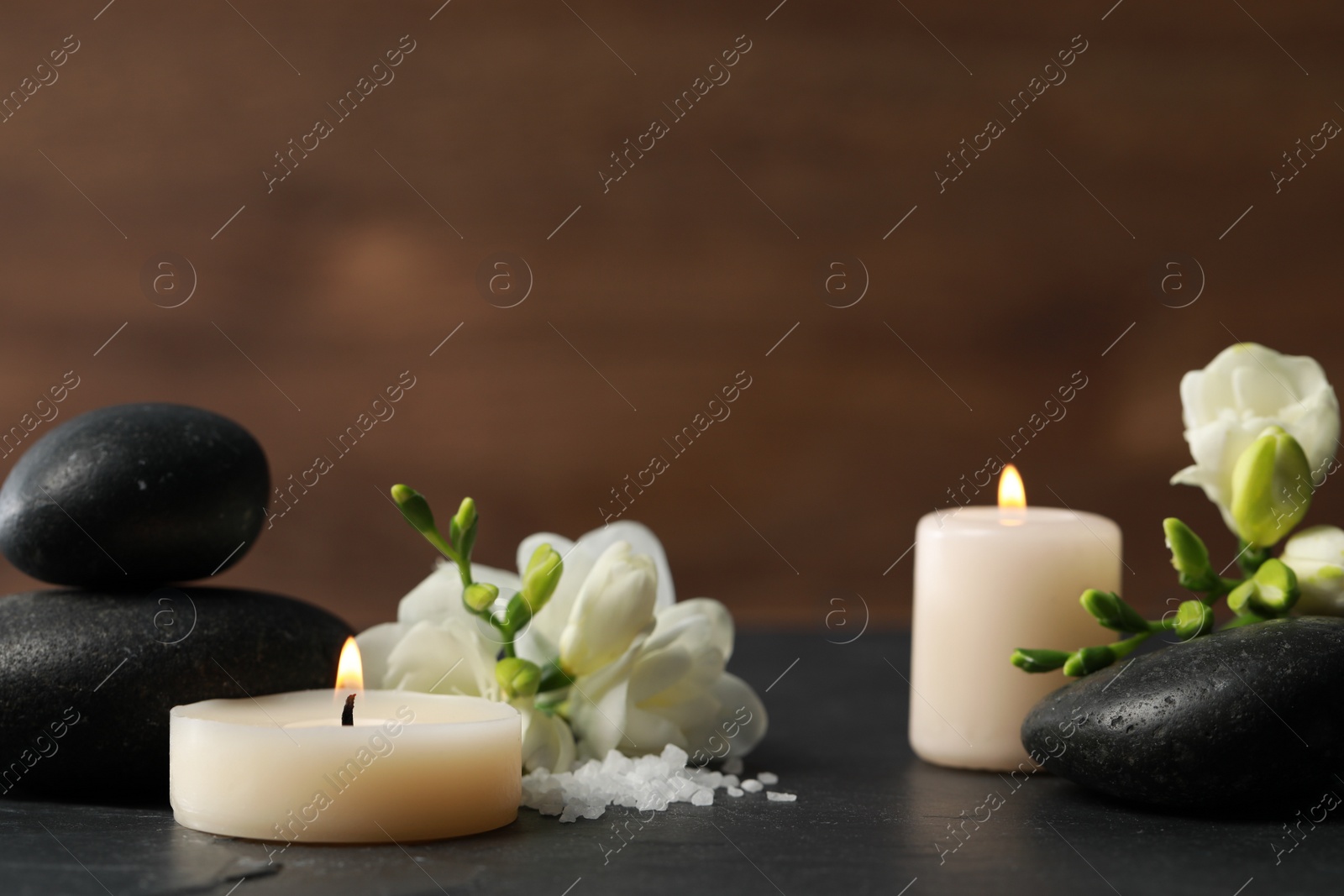 Photo of Beautiful composition with spa stones, burning candles and flowers on black table. Space for text