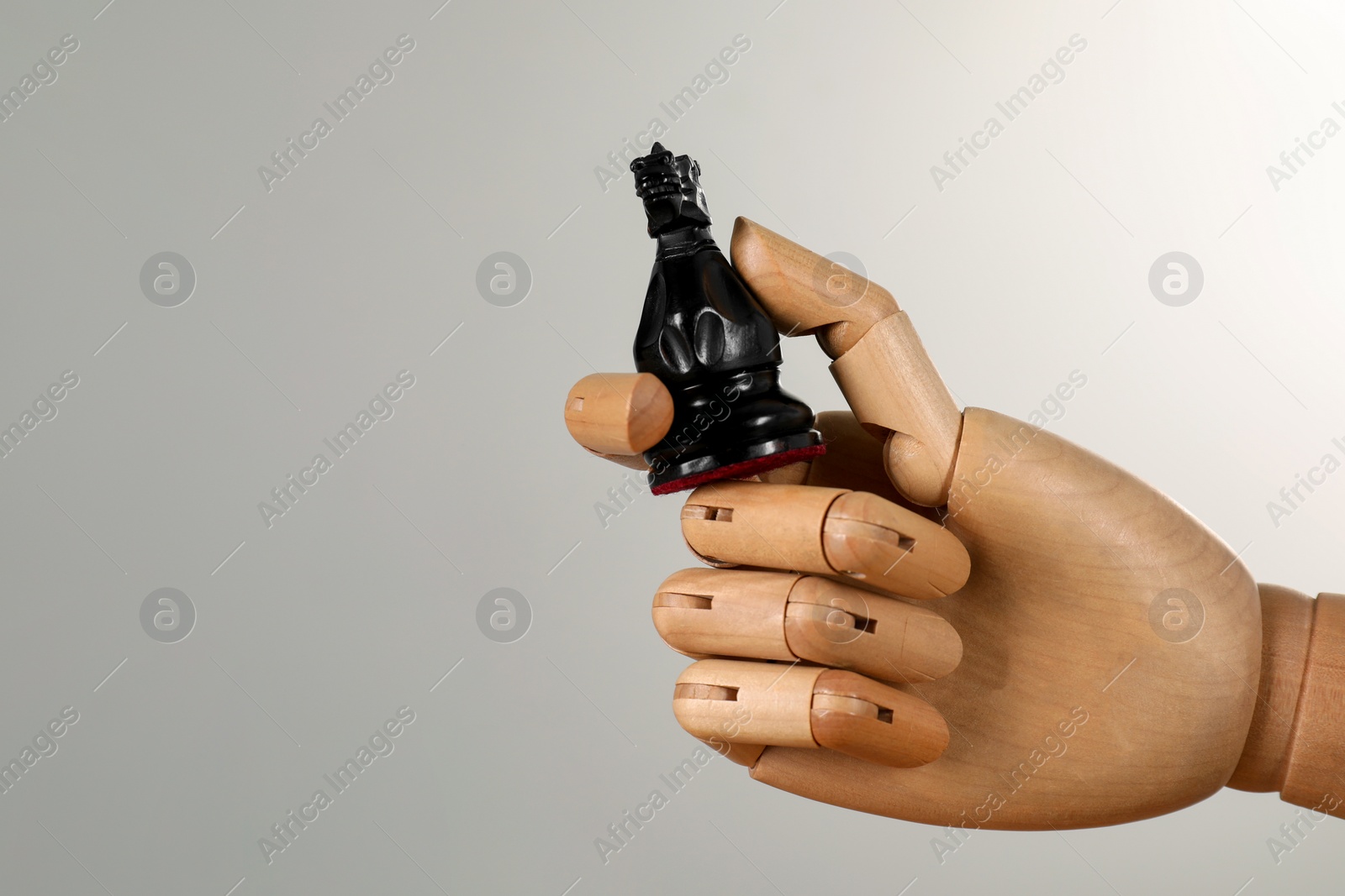 Photo of Robot with chess piece against light grey background, space for text. Wooden hand representing artificial intelligence