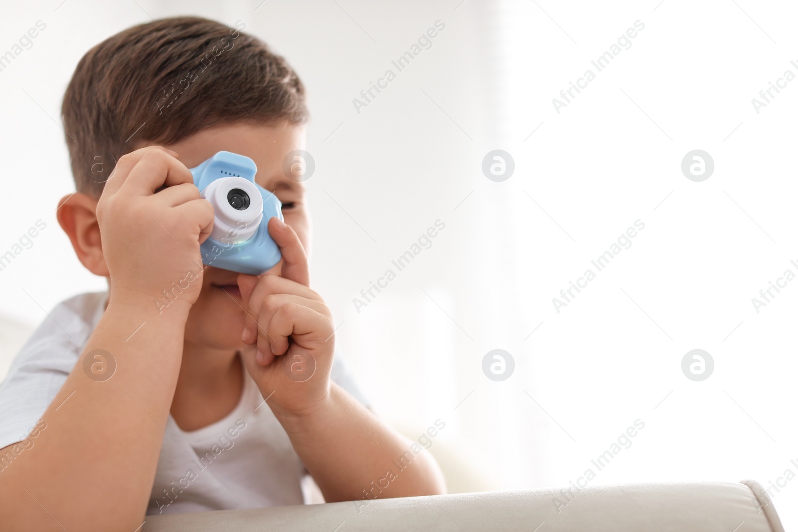 Photo of Little photographer taking picture with toy camera on sofa at home. Space for text