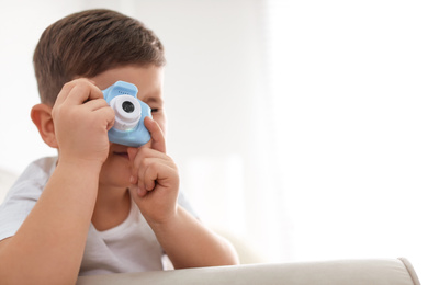 Little photographer taking picture with toy camera on sofa at home. Space for text