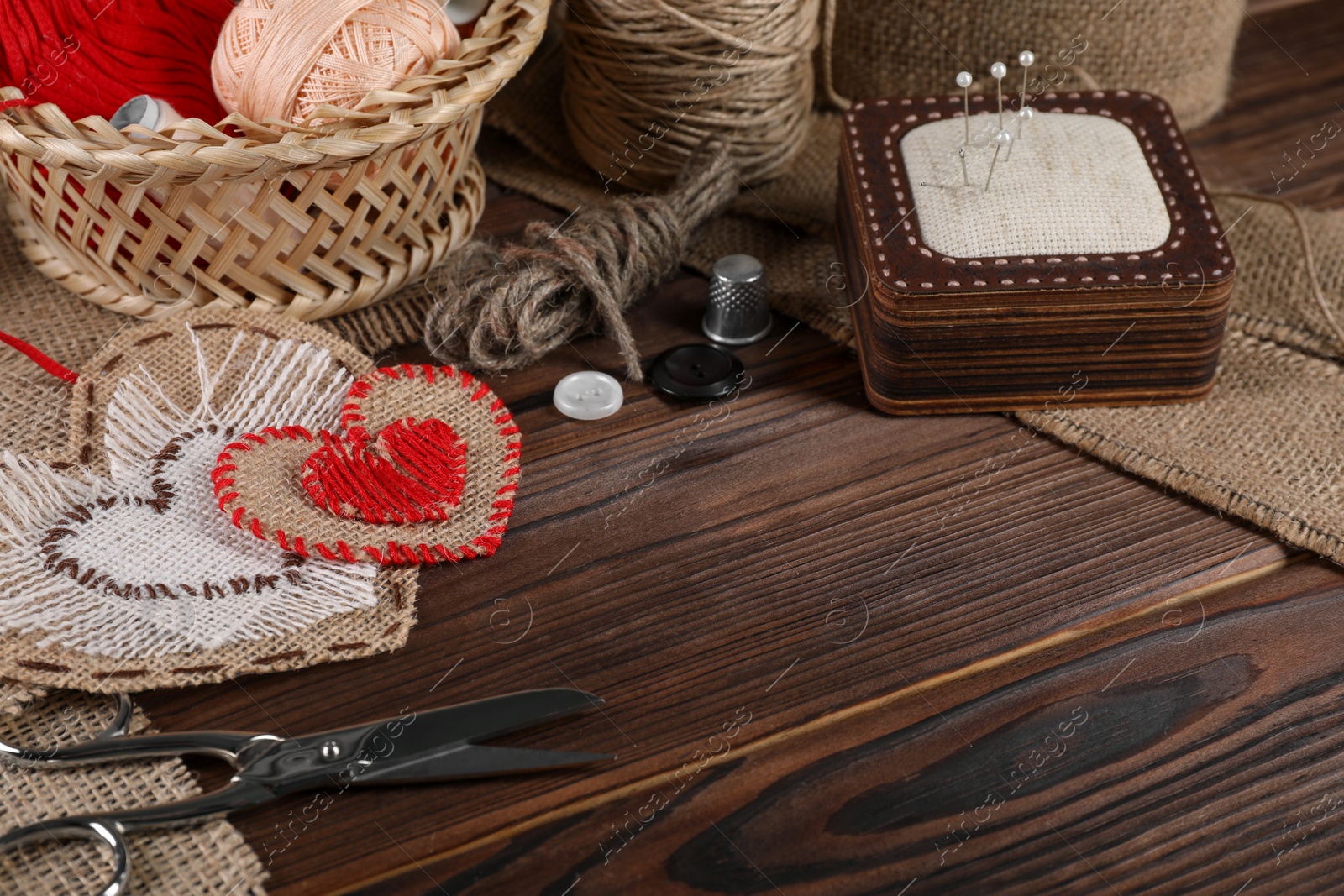 Photo of Heart shaped pieces of burlap fabric with different stitches and sewing tools on wooden table, closeup. Space for text