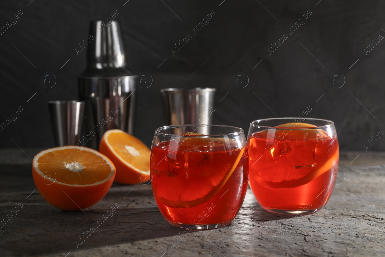 Photo of Aperol spritz cocktail, ice cubes and orange slices in glasses on grey textured table