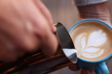 Photo of Barista pouring milk into cup of coffee, closeup