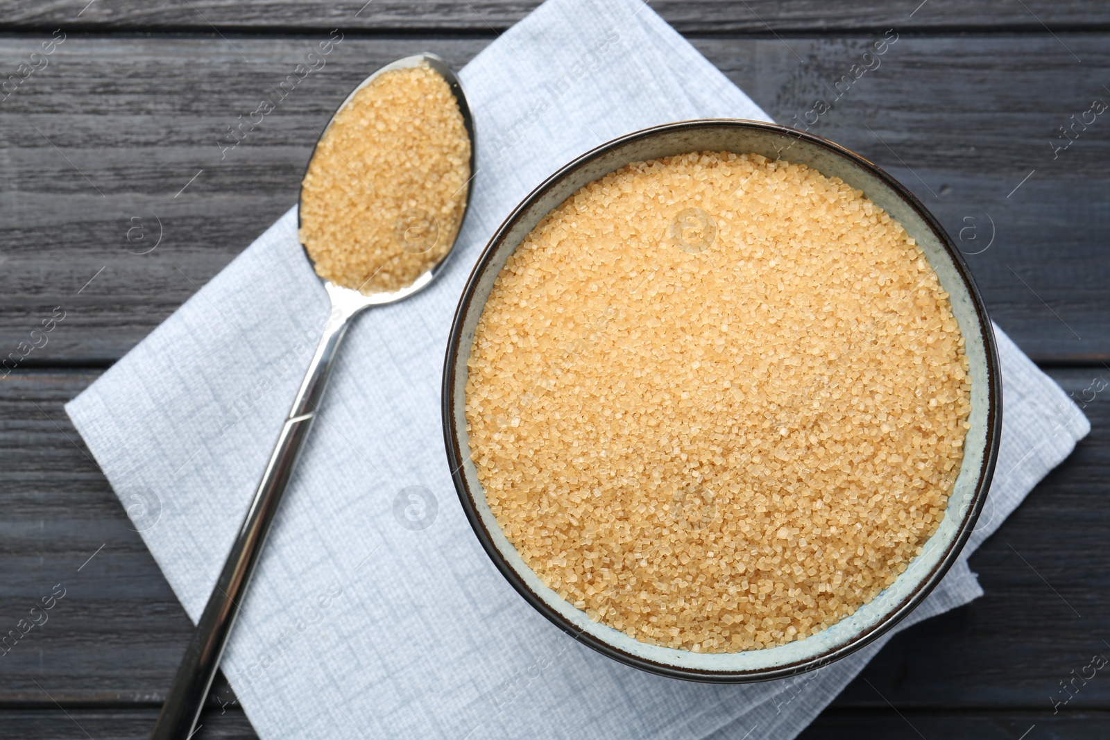 Photo of Brown sugar in bowl and spoon on black wooden table, flat lay