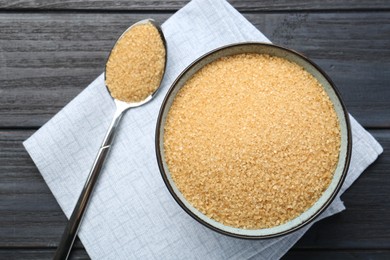 Photo of Brown sugar in bowl and spoon on black wooden table, flat lay