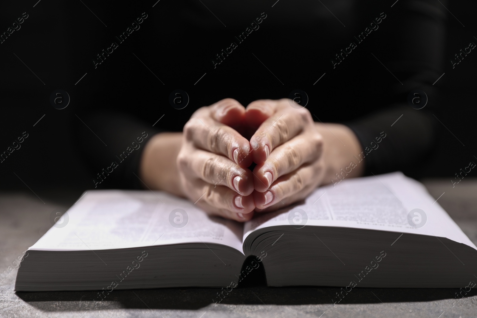 Photo of Religion. Christian woman praying over Bible at table, closeup