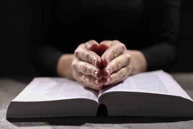 Photo of Religion. Christian woman praying over Bible at table, closeup