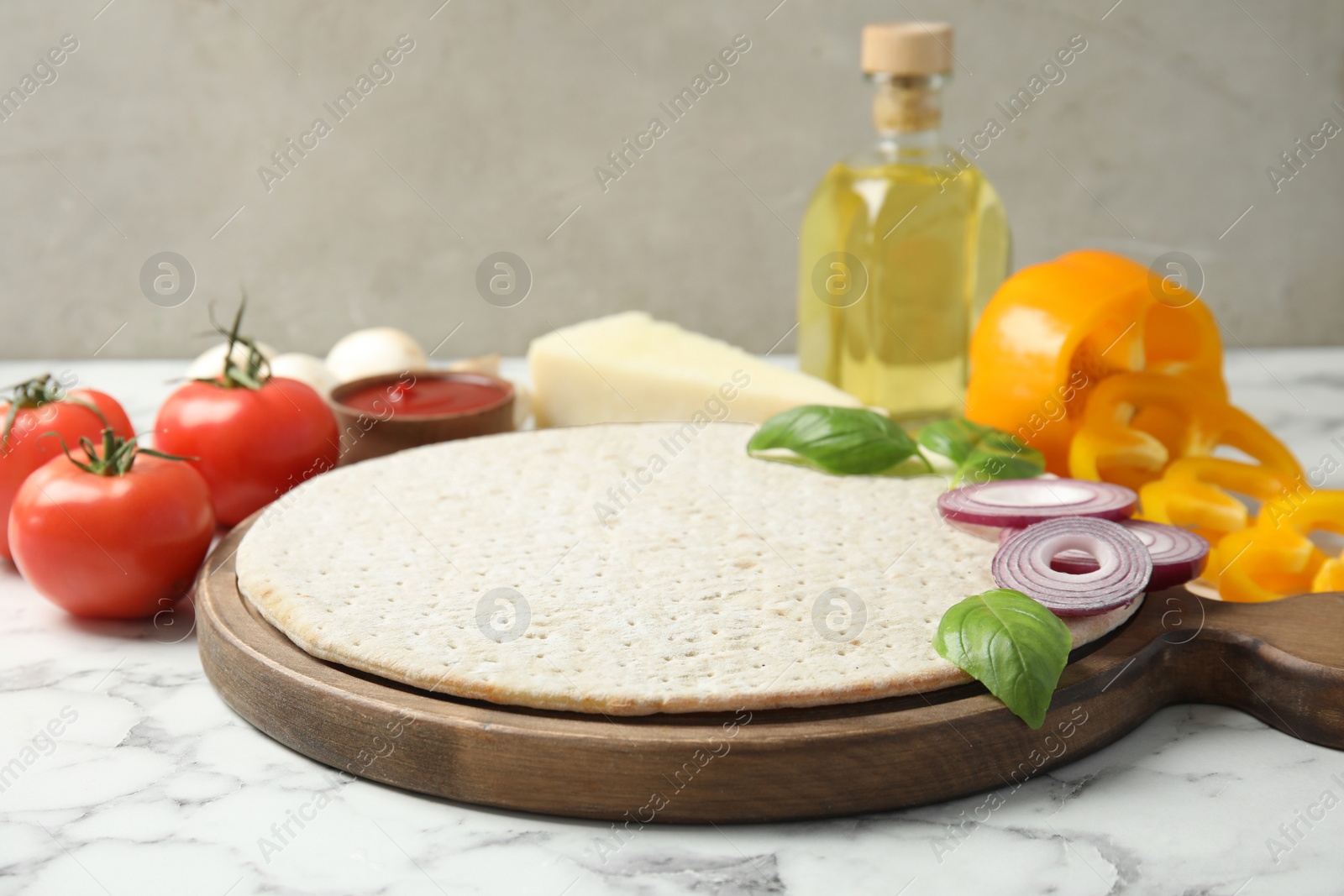 Photo of Base and ingredients for pizza on marble table against light background