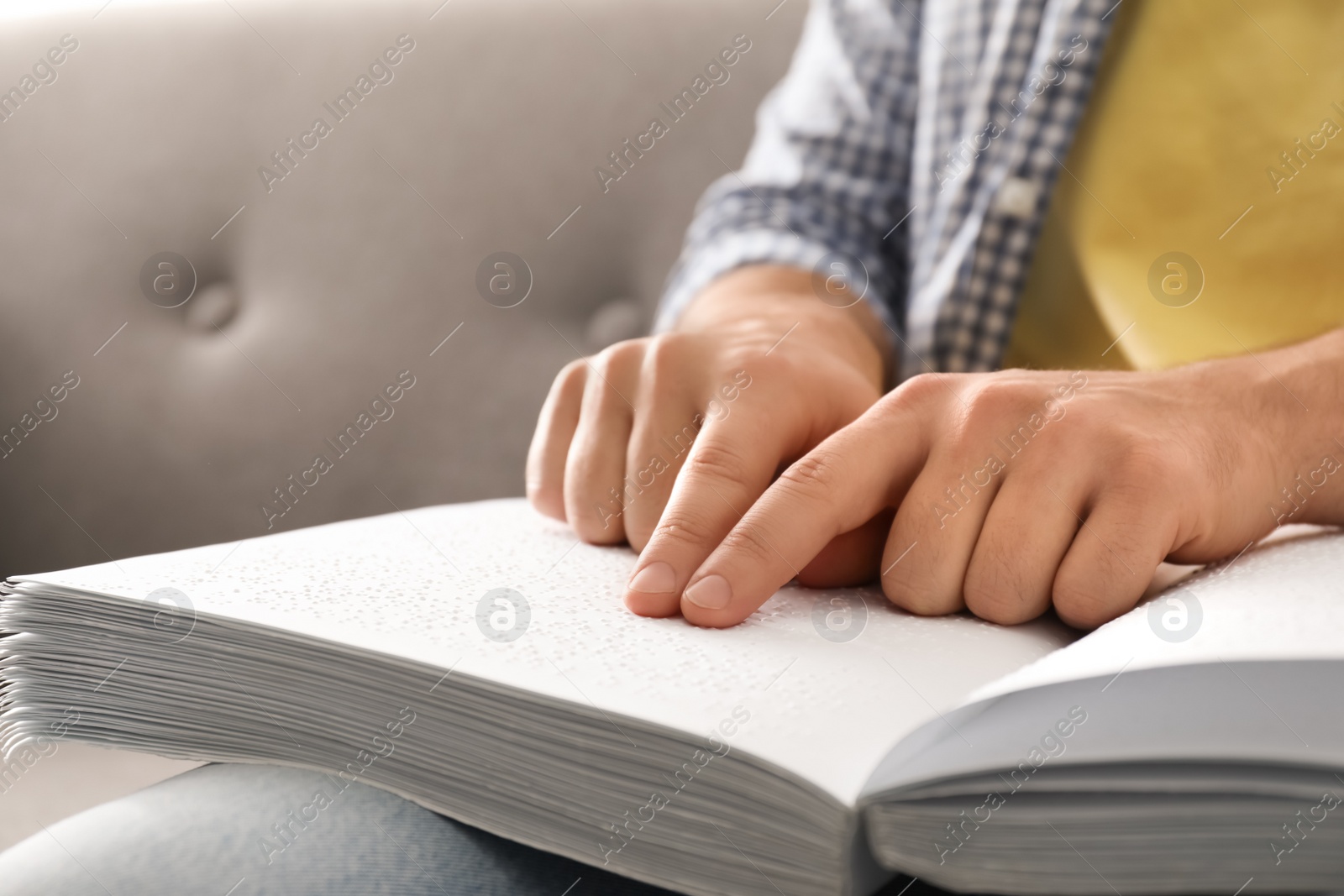 Photo of Blind man reading book written in Braille on sofa, closeup