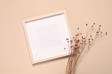 Empty photo frame and dry decorative flowers on beige background, flat lay. Space for design