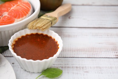 Photo of Fresh marinade, fish and brush on white wooden table, closeup. Space for text